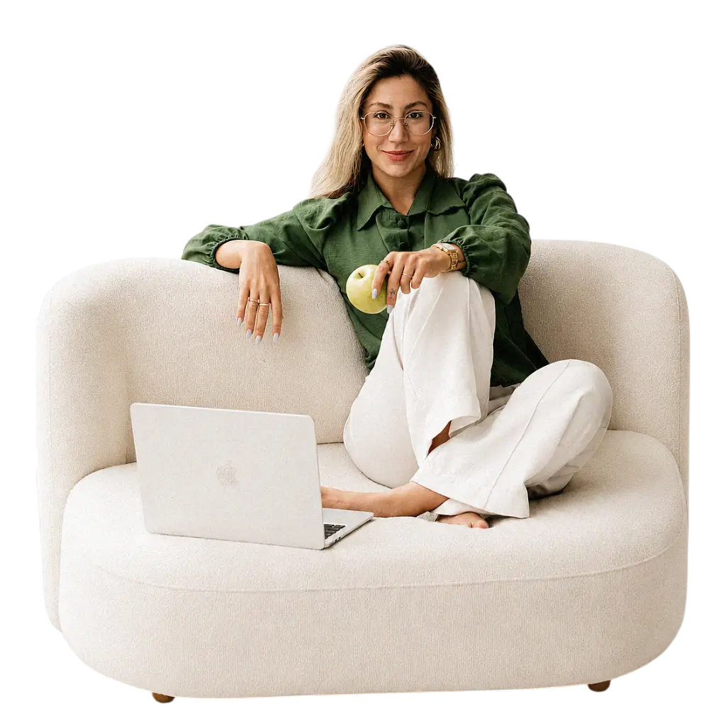 Mariana Sander, nutricionista, sentada em um sofá com uma maçã e um notebook.